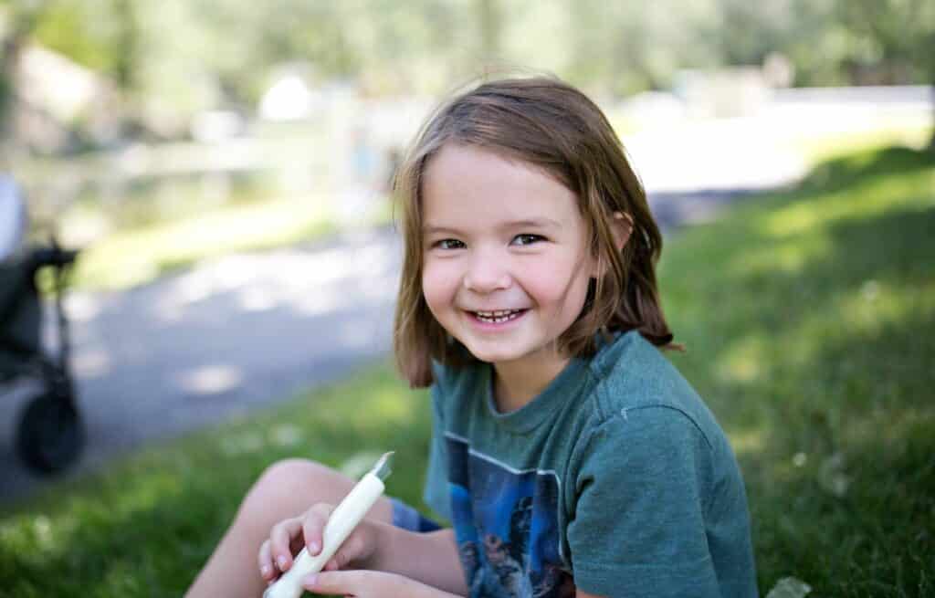 A child with brown hair smiles and holds a cheese stick