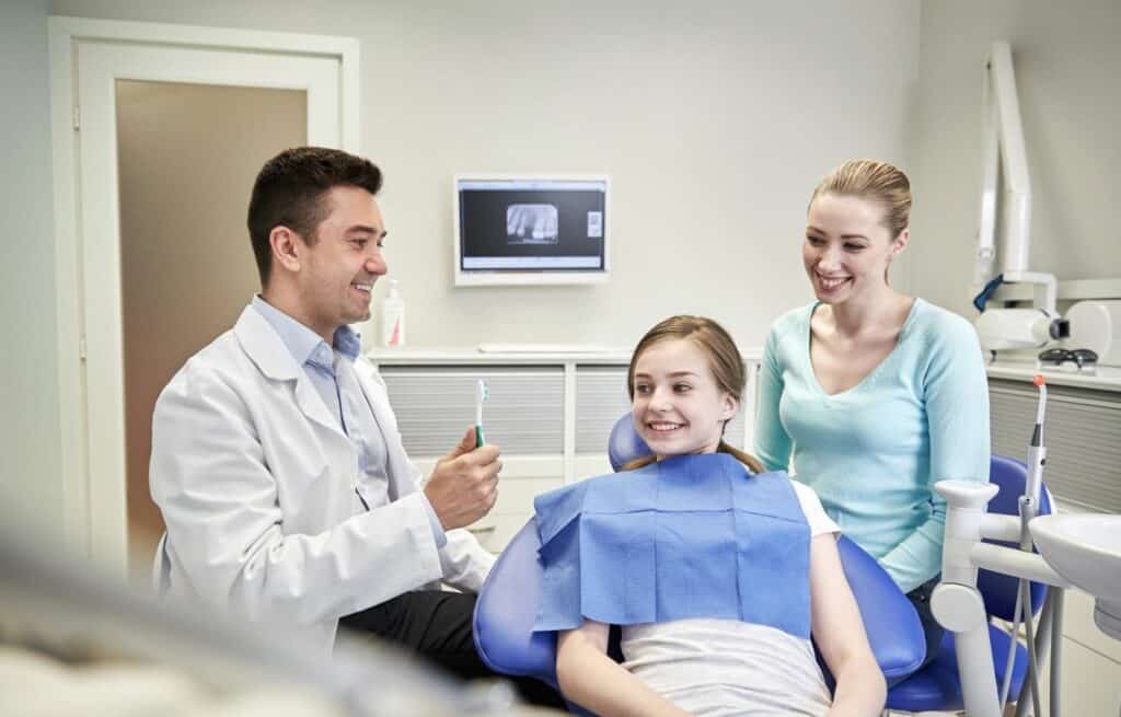 A young patient and her mother talk to a male dentist